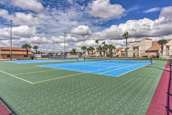 Play a game of tennis under the open sky on this outdoor tennis court surrounded by lush palm trees and safety zones.