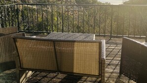 Ein Balkon mit Korbmöbeln, der auf ein Gewässer und ferne Hügel blickt.