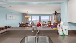 A modern kitchen with a double sink, a dining area with a table and chairs, and a view of the ocean through large windows. - Gulf Front Living Room AND Master Suite! Sleeps 8! (Panama City Beach)