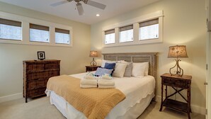 Une chambre à coucher avec un grand lit, deux tables de chevet avec des lampes, une commode en bois et un ventilateur de plafond.