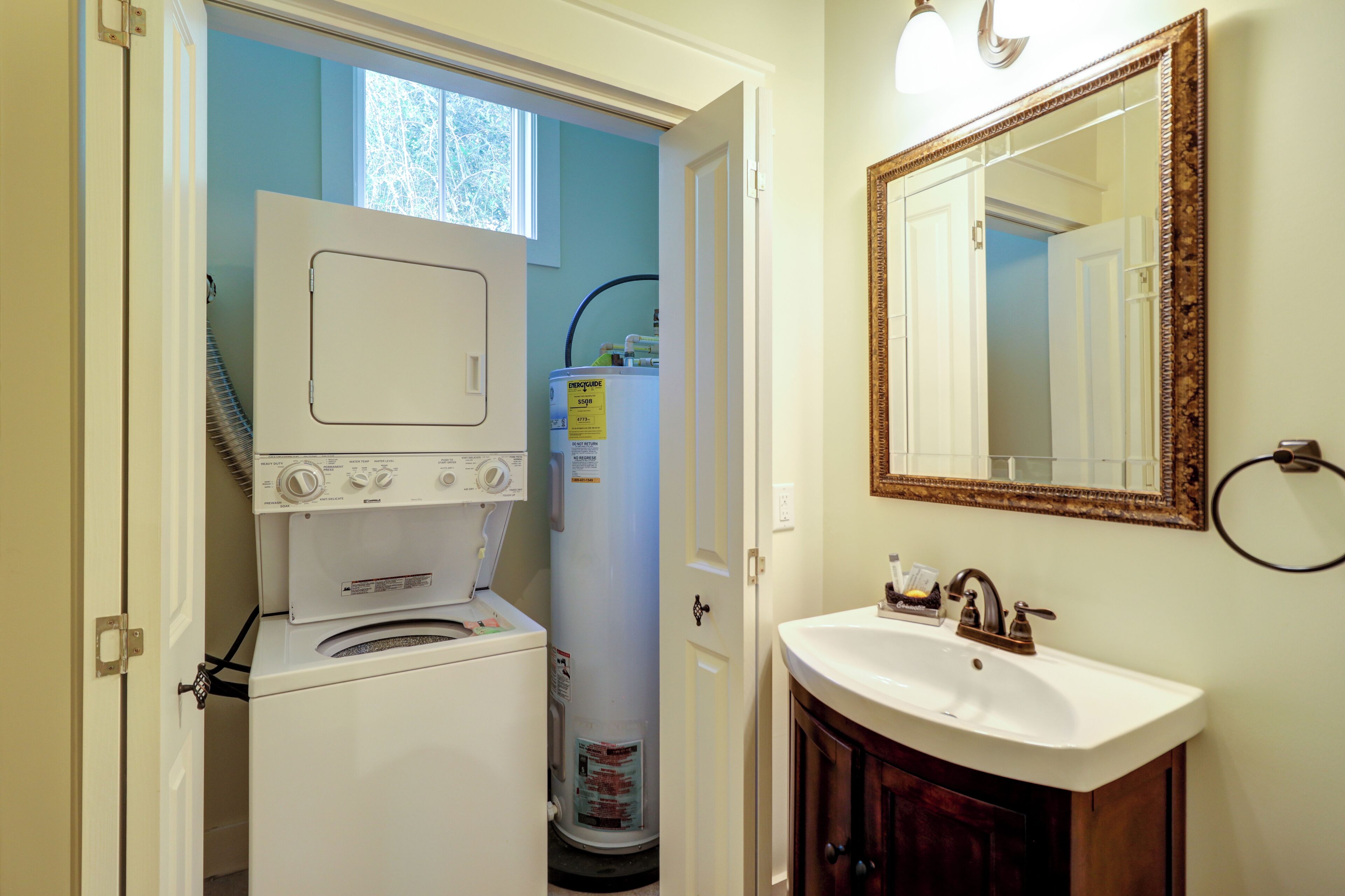 A compact laundry room with a washer and dryer, a water heater, and a sink with a mirror above it.