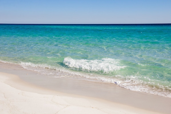 Enjoy a tranquil beach experience with clear waters gently lapping onto the sandy shore.