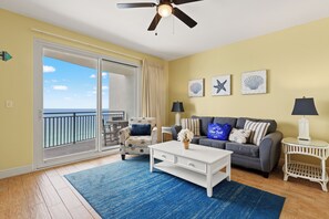 Una sala de estar con sofá, mesa de centro y sillón, un balcón con vistas y decoración en la pared.