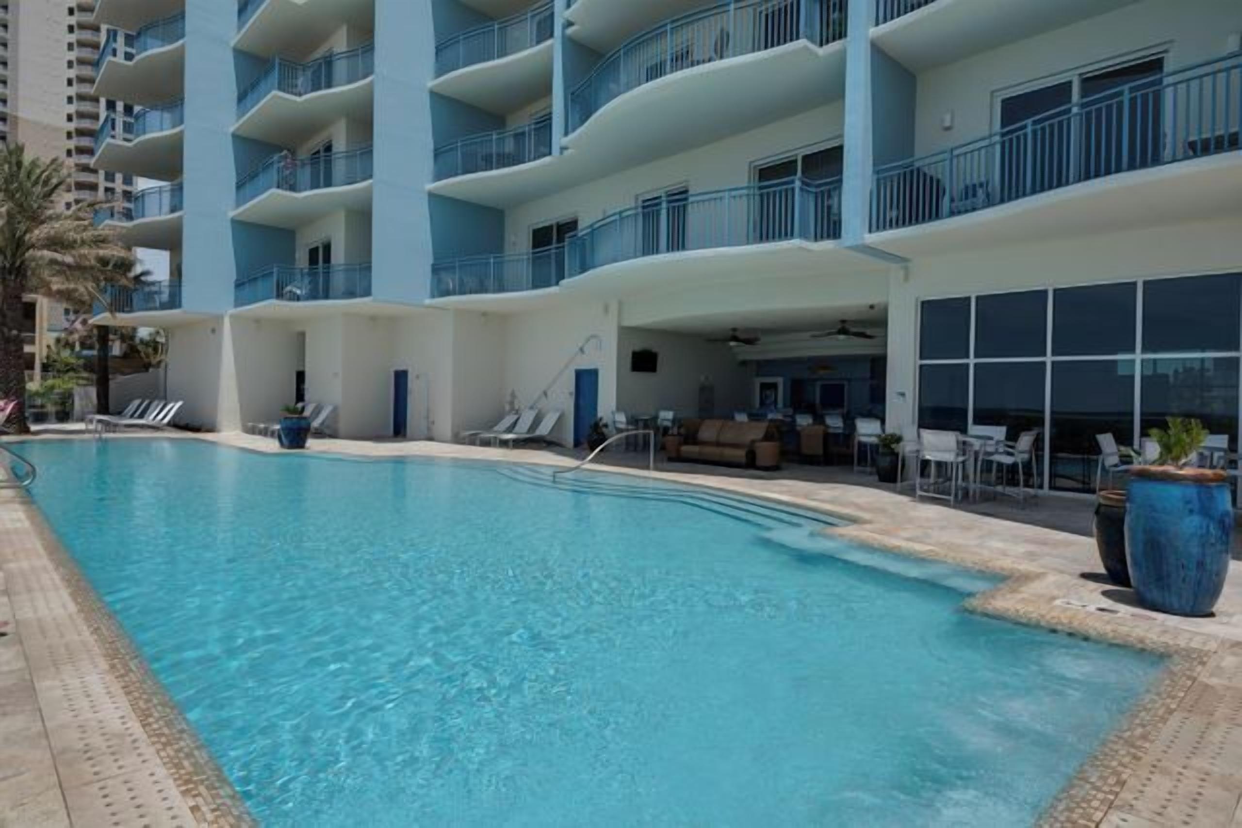 A swimming pool with lounge chairs and a seating area, surrounded by a multi-story building with balconies.