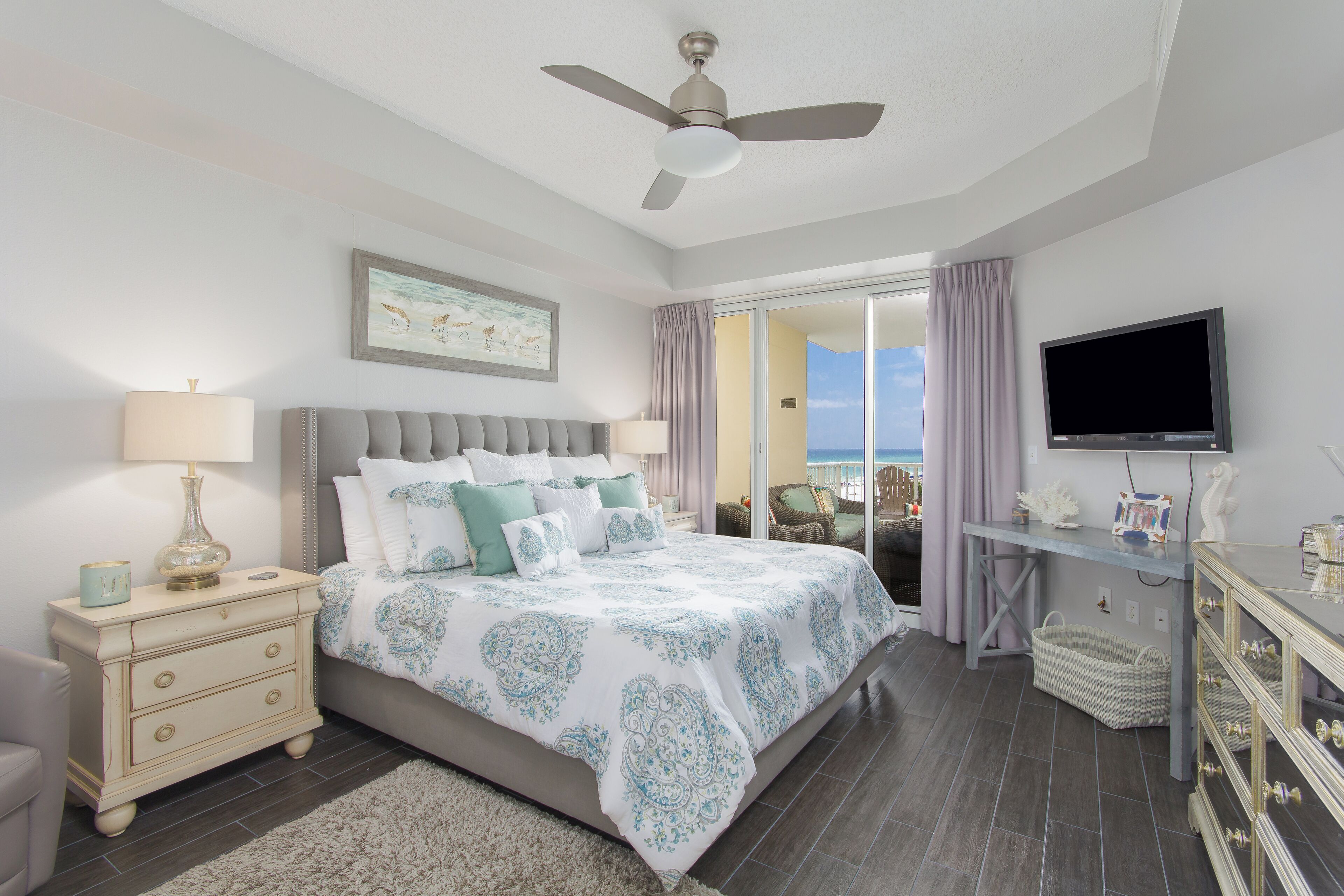 A bedroom with a bed, nightstand, dresser, TV, and a view of the outdoors.
