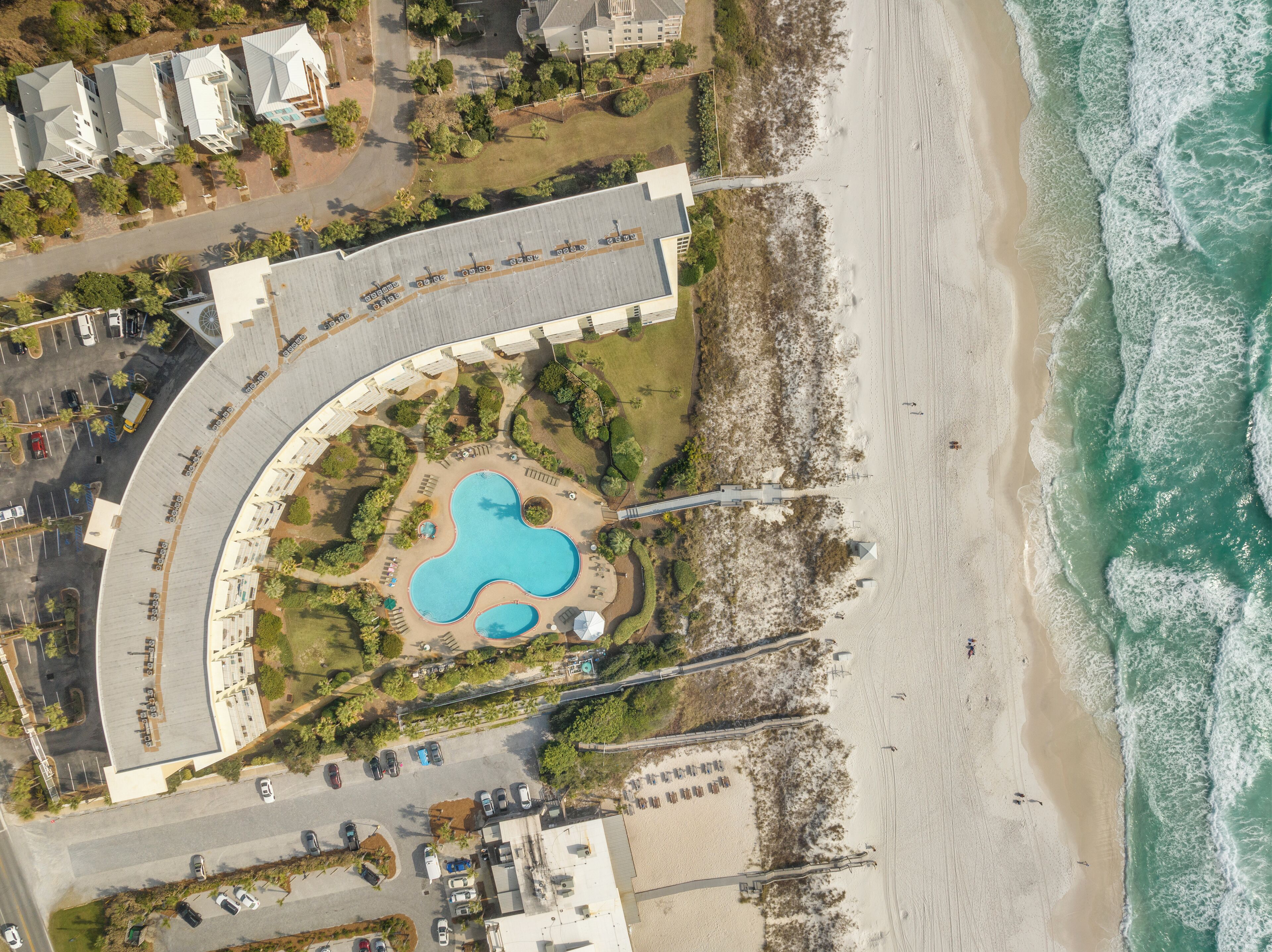 An aerial view of a resort with a curved pool, beach access, and a parking area.