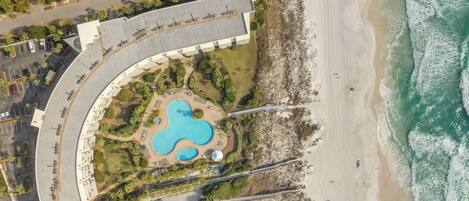 An aerial view of a resort with a curved pool, beach access, and a parking area.