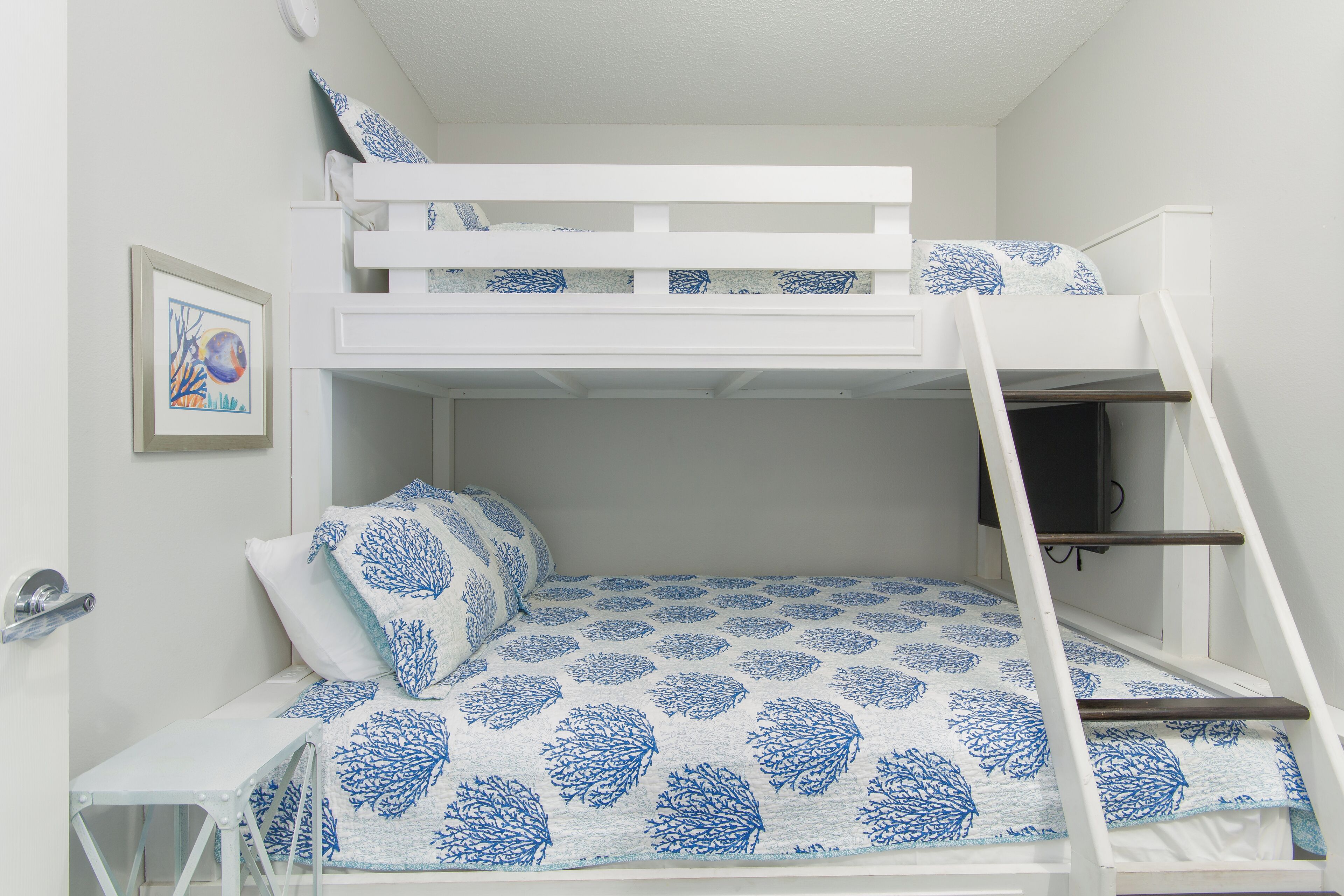 A bunk bed with a ladder, a small table, and a framed picture on the wall.