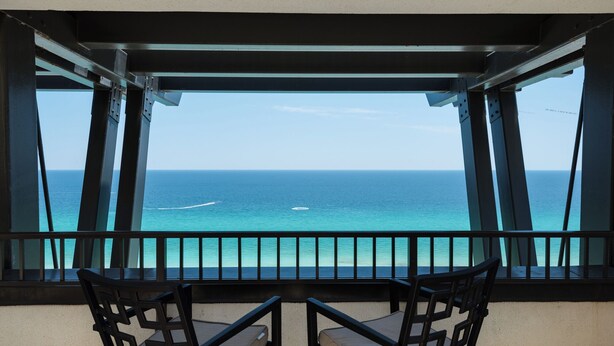 A balcony with two chairs facing a view of the ocean.
