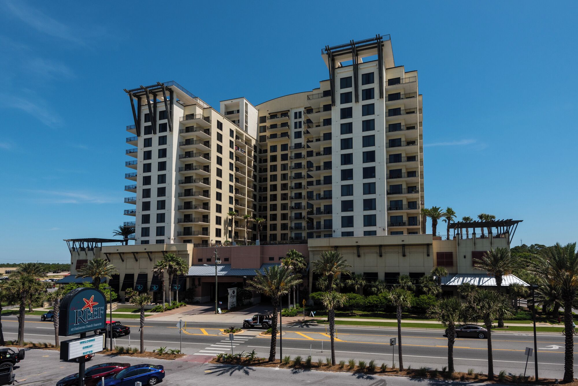 A multi-story hotel with a modern architectural design, featuring balconies on each floor and a prominent entrance with a sign.