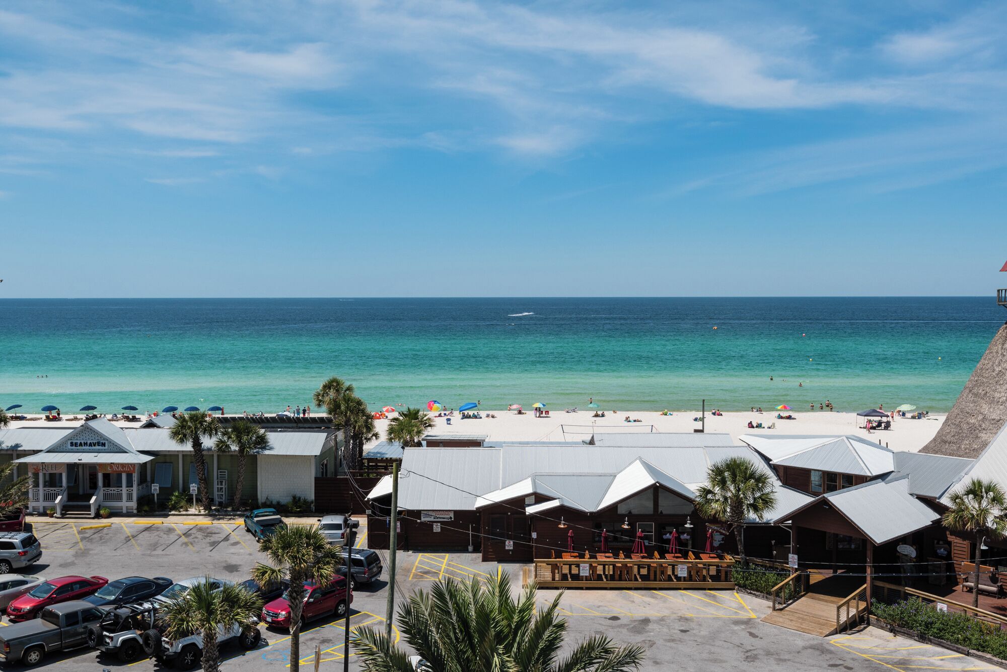 Vista a la playa con un restaurante y zona de estacionamiento.