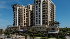 A multi-story hotel with balconies, a covered entrance, and palm trees in the foreground.
