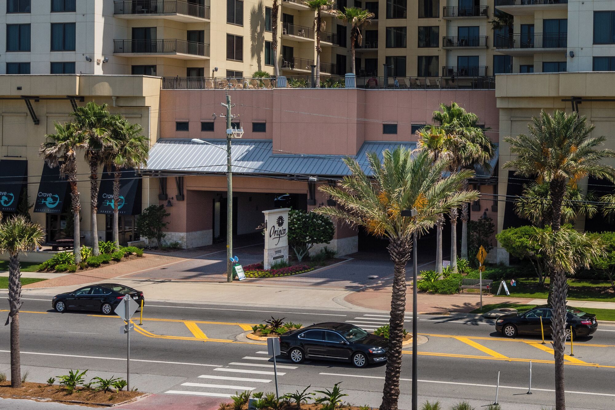 A hotel entrance with a covered driveway, palm trees, and a crosswalk.