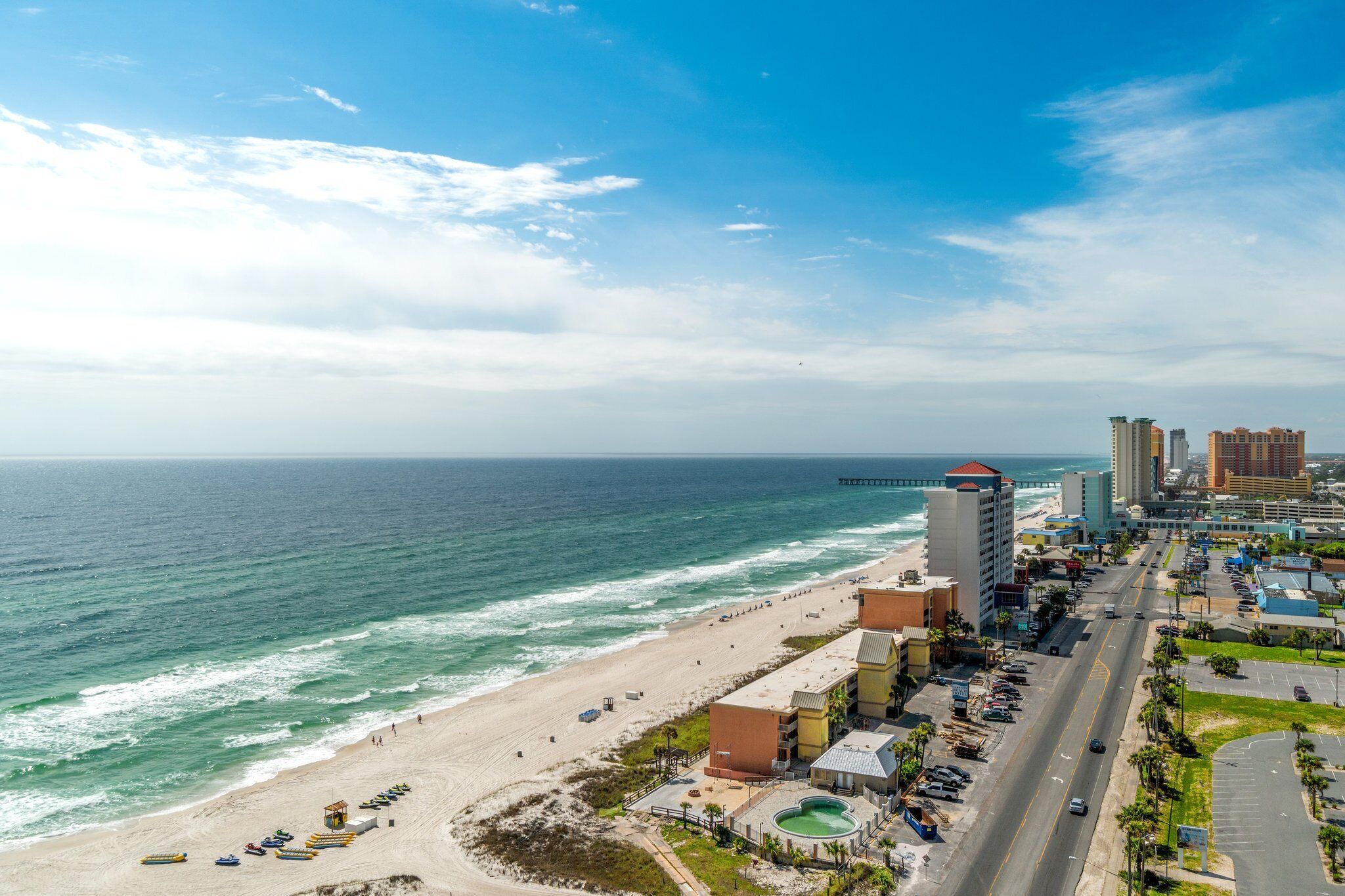 A coastal cityscape with a beach, a pier, and high-rise buildings.