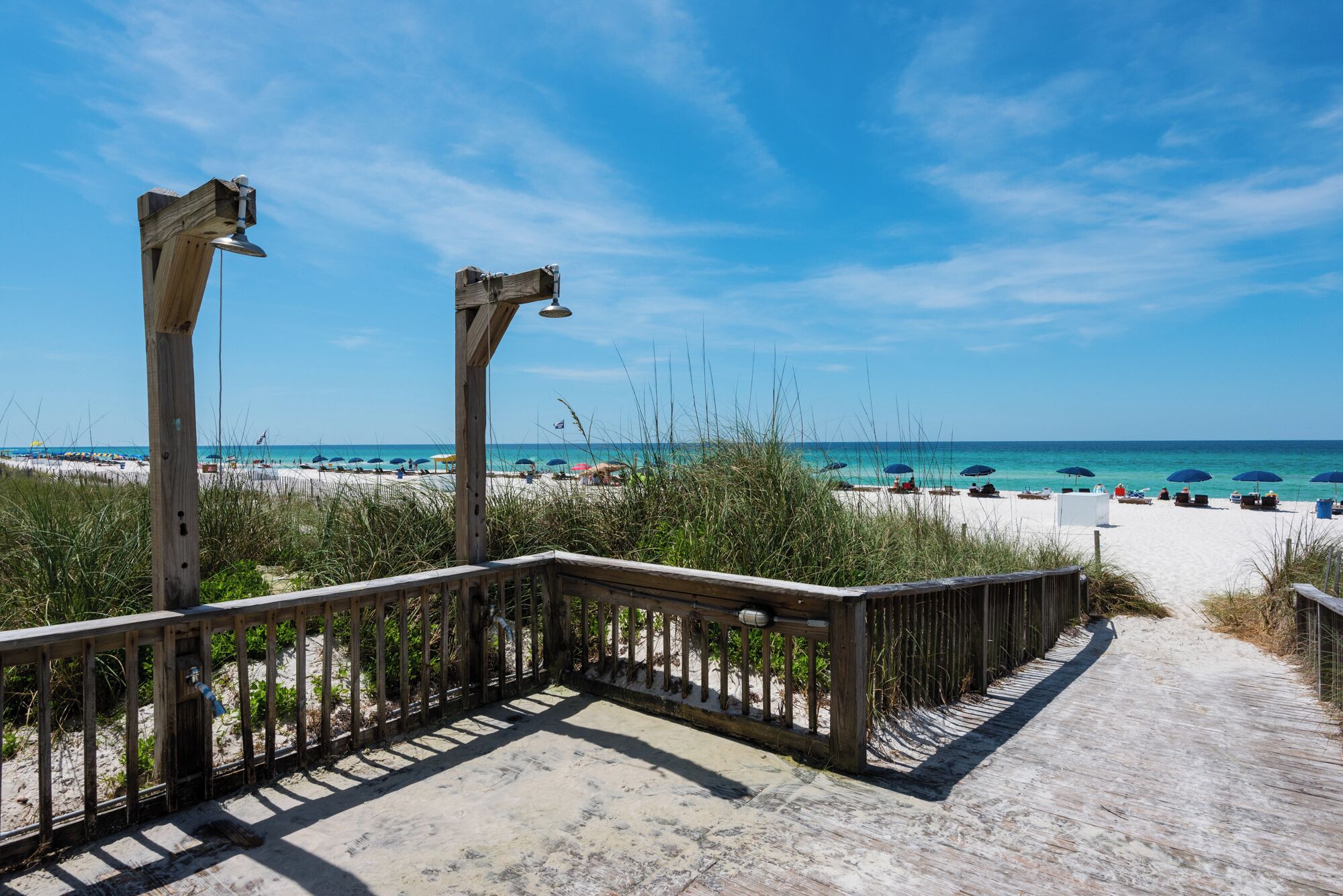 A wooden boardwalk leading to a beach with umbrellas and people.
