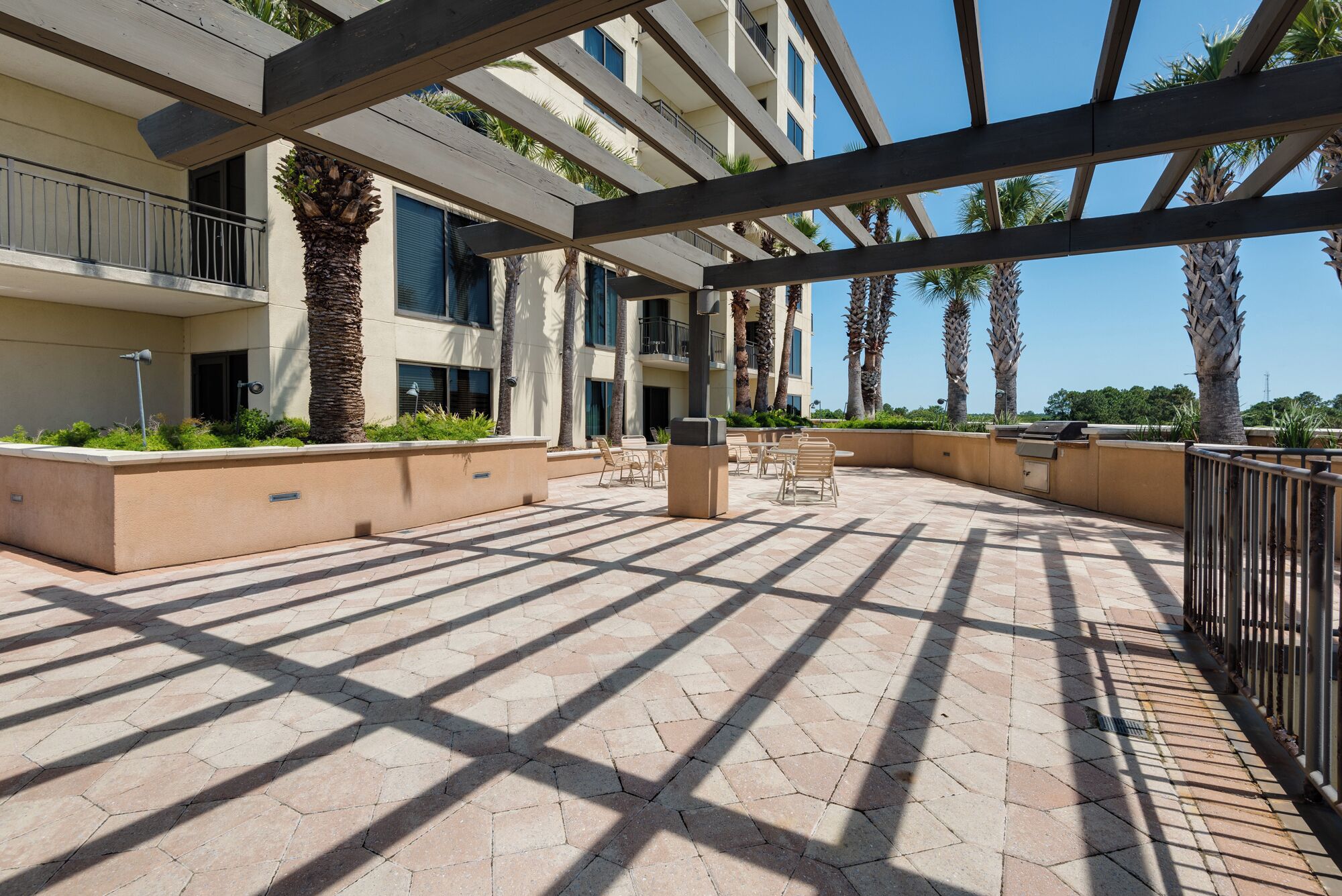 An outdoor patio area with hexagonal tiles, outdoor seating, and palm trees.