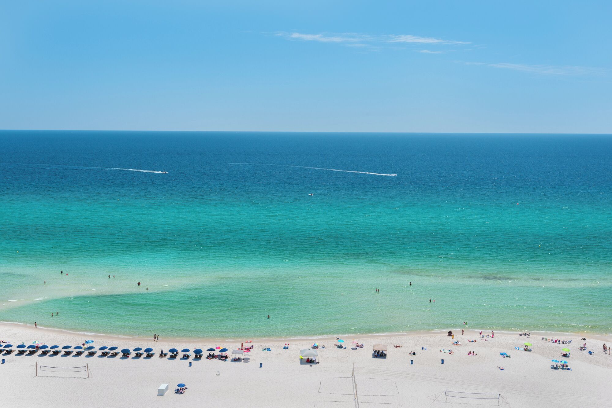 A beach with clear turquoise waters, a volleyball net, and beach umbrellas.
