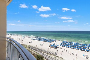 Une plage bordée de rangées de parasols bleus et de chaises longues, une étendue de sable et l’océan.
