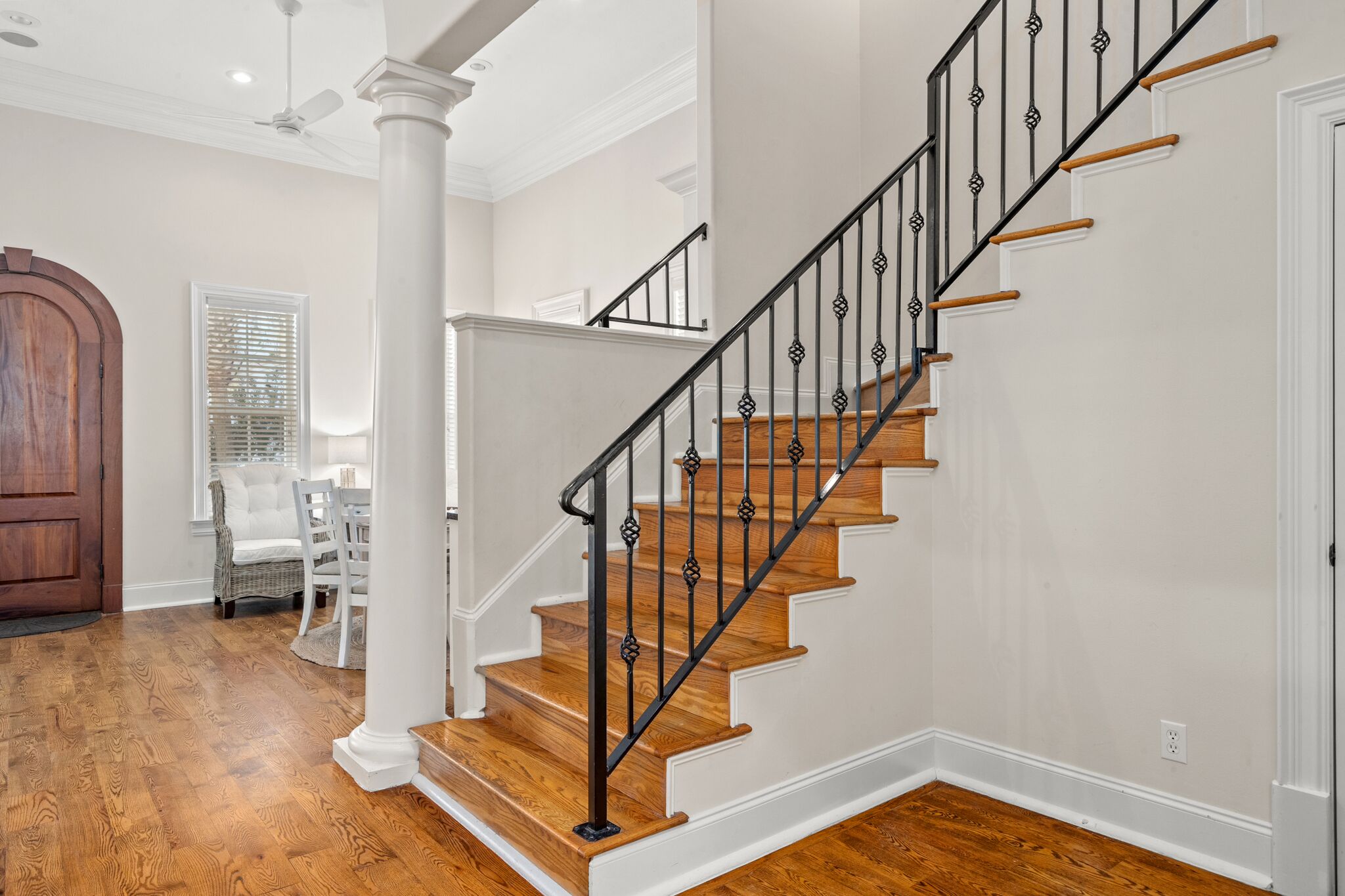 A staircase with wooden steps and black metal railings, white walls, and a wooden door.