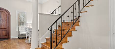 A staircase with wooden steps and black metal railings, white walls, and a wooden door.