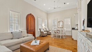 A spacious living room with a beige sofa, a brown ottoman, and a dining area with a white table and chairs. - Luxury Home Steps From Beach in Gated Community (Santa Rosa Beach)