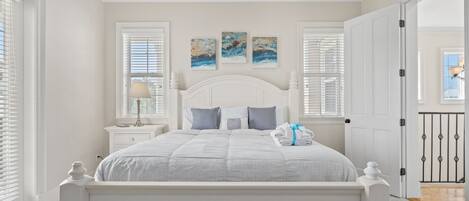 A bedroom with a white bed, two nightstands, a lamp, and artwork on the wall.