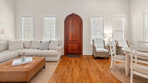 A living room with a beige sofa, a wooden door, and wicker chairs. - Luxury Home Steps From Beach in Gated Community (Santa Rosa Beach)