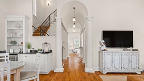 A spacious living area with a wooden floor, white cabinetry, a staircase, and a large flat-screen TV. - Luxury Home Steps From Beach in Gated Community (Santa Rosa Beach)