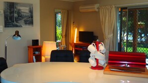 Een moderne woonkamer met een ronde witte tafel, een televisie en een raam met gordijnen.