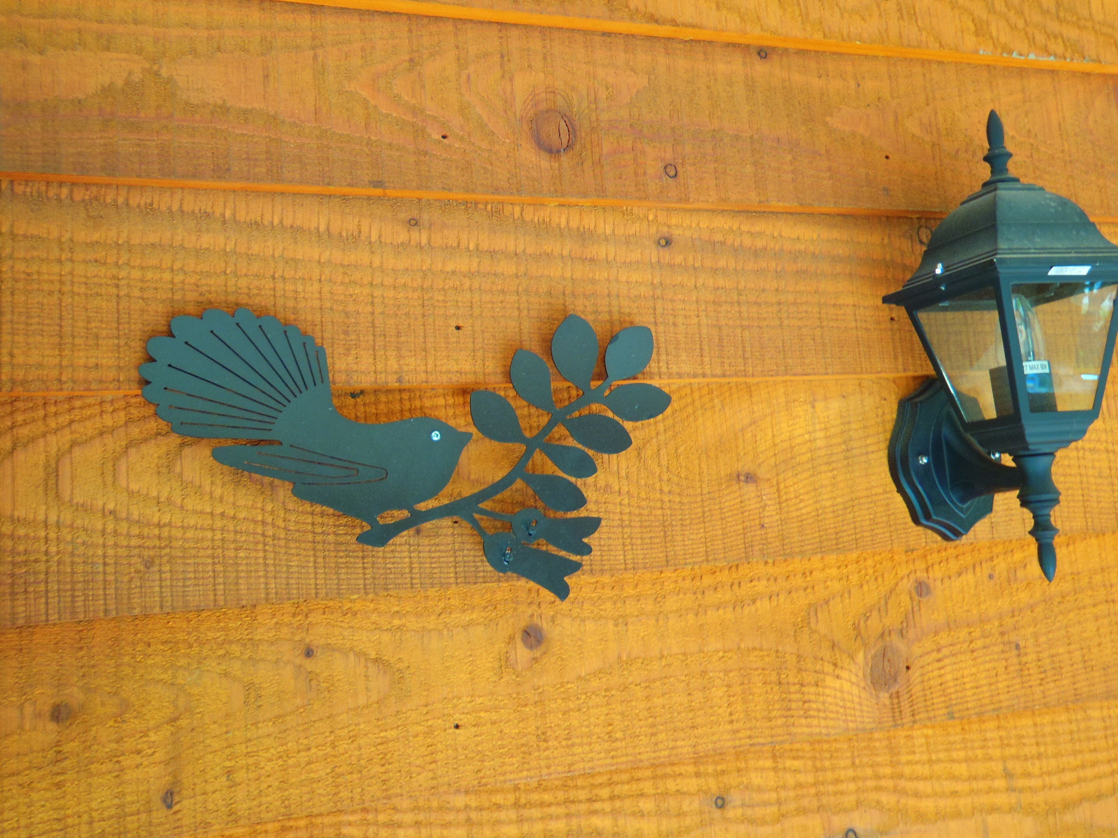 Un mur en bois orné d’une décoration métallique en forme d’oiseau et d’une lanterne fixée au mur.