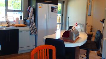 A compact kitchen with a refrigerator, sink, and a small dining area with a chair and table.