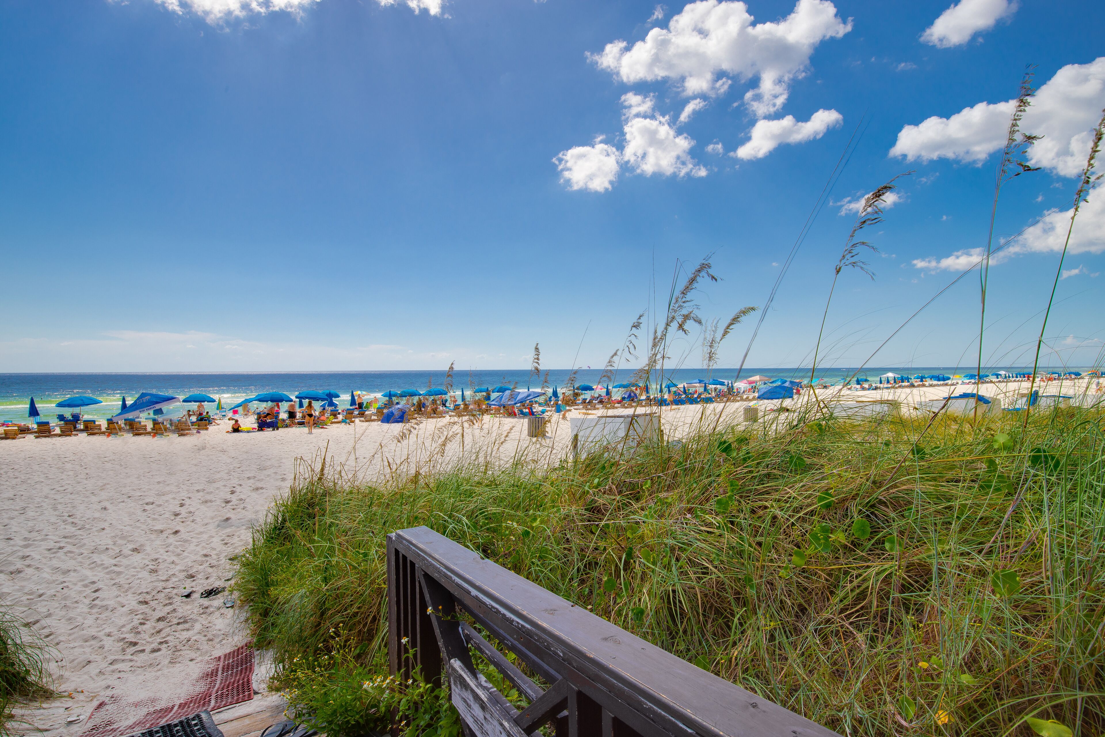 A beach with a wooden boardwalk, beach umbrellas, and lounge chairs.