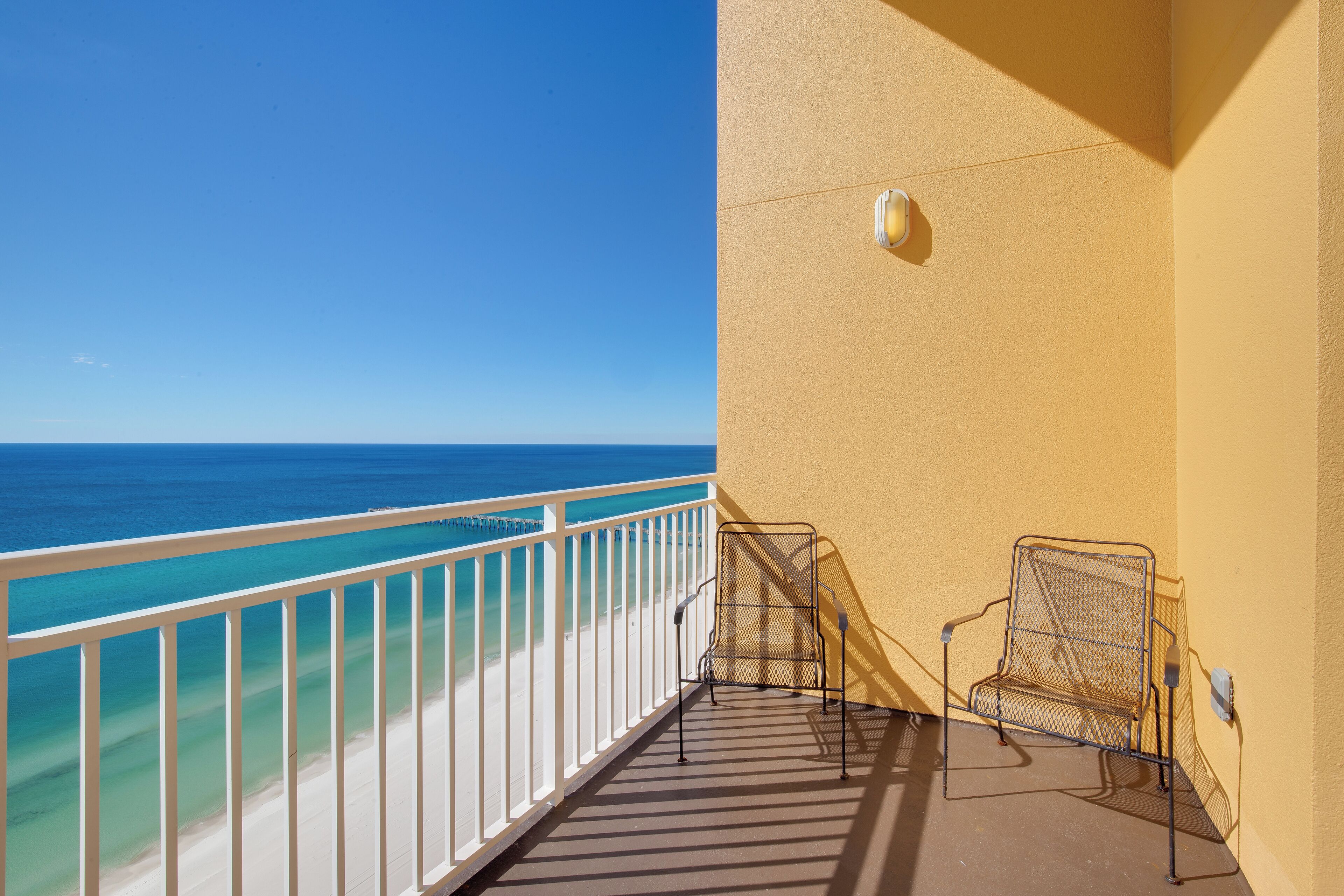 Un balcón con una silla de metal y baranda blanca con vista a la playa.