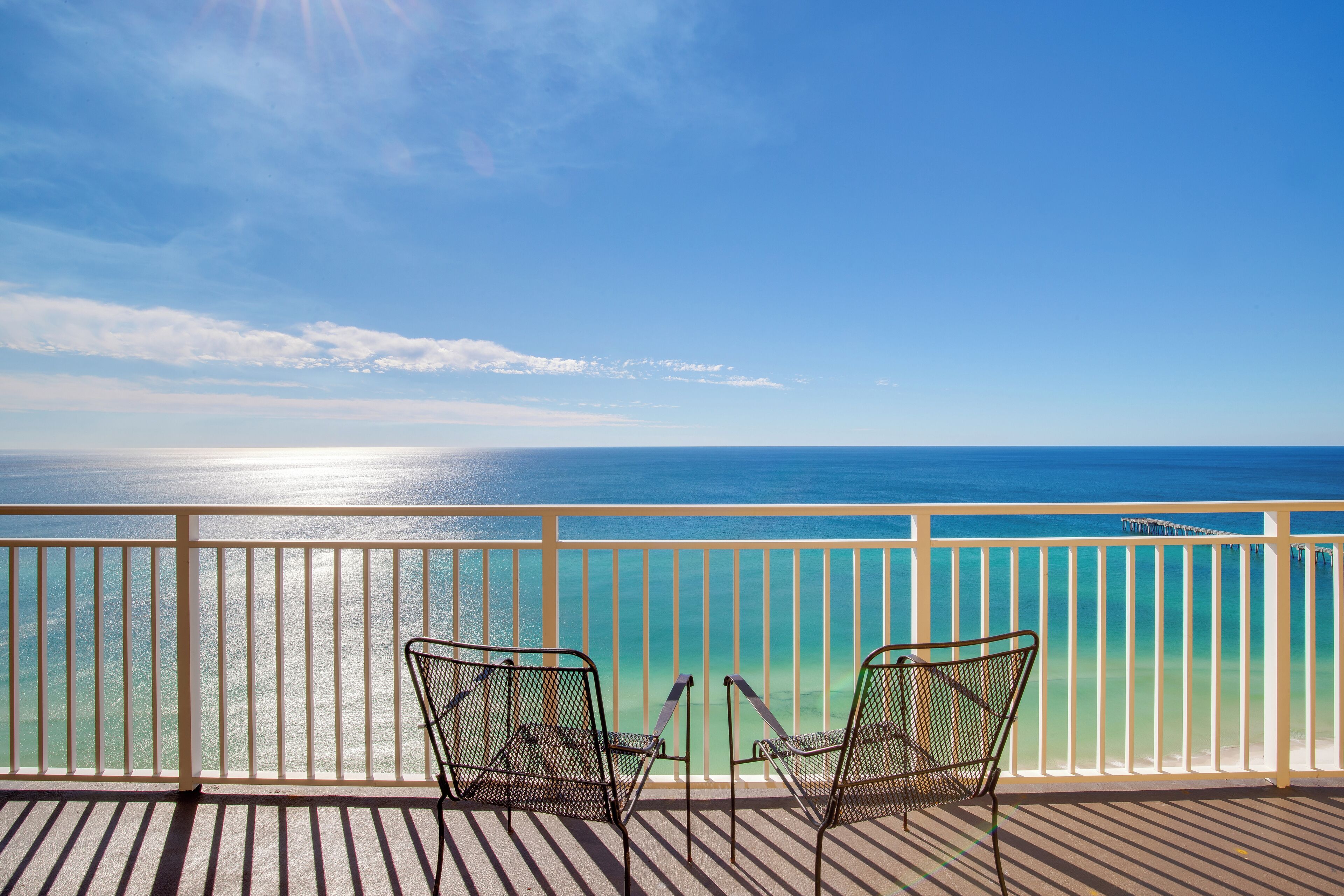 Un balcon avec deux chaises en métal donnant sur une mer turquoise.