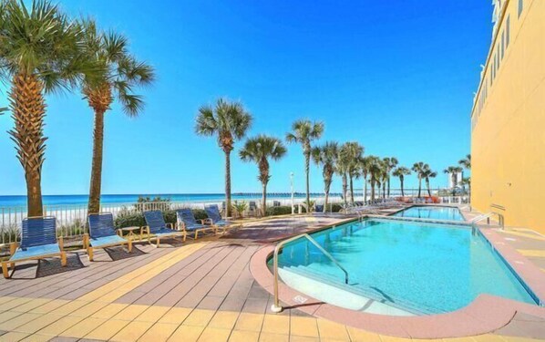 A poolside area with lounge chairs and palm trees, overlooking a clear blue sky and ocean. - Penthouse! Beautiful Views! Newly Remodeled and Listed! (Panama City Beach)
