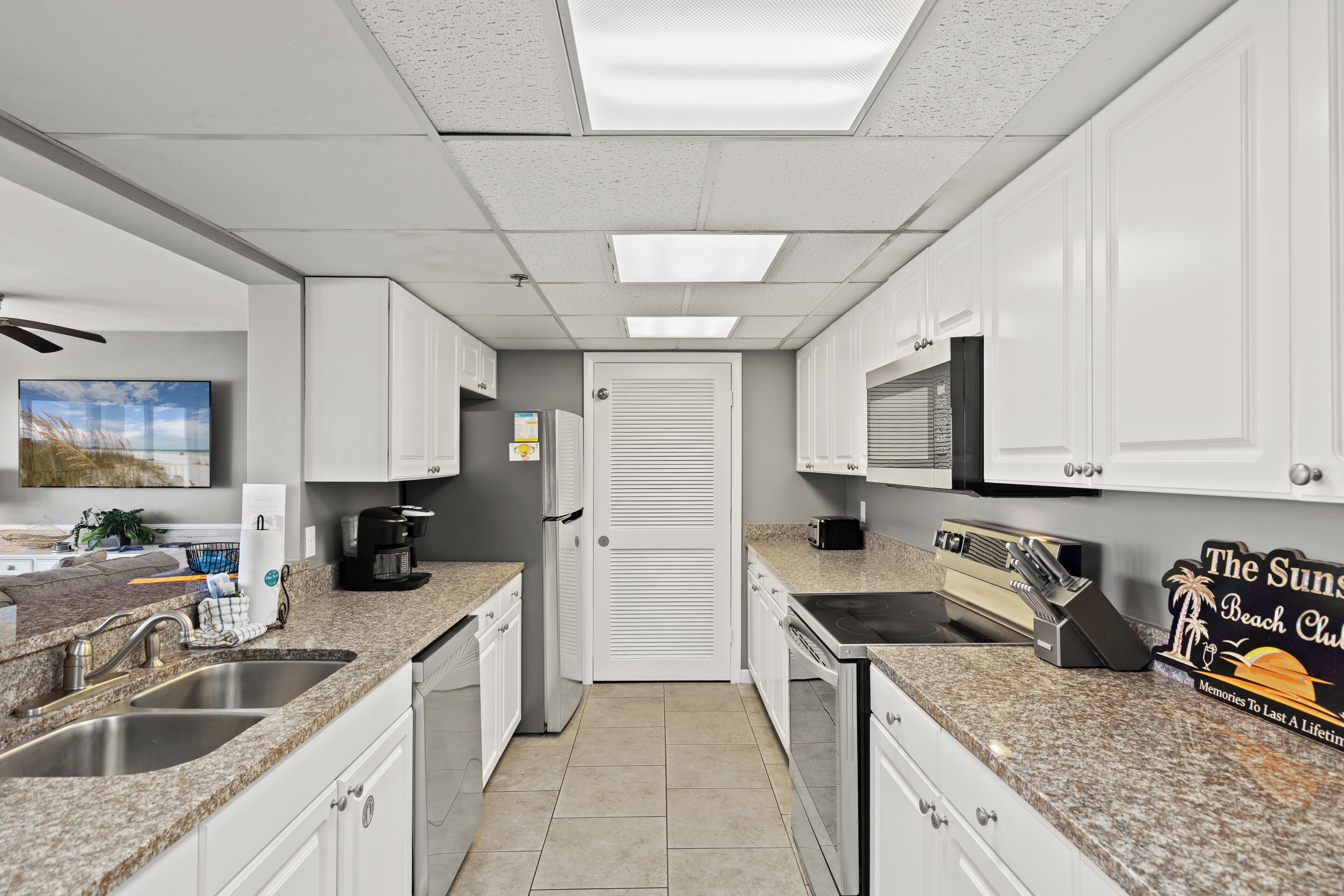 A kitchen with white cabinets, granite countertops, a coffee maker, and a sign for 'The Sun Club.'