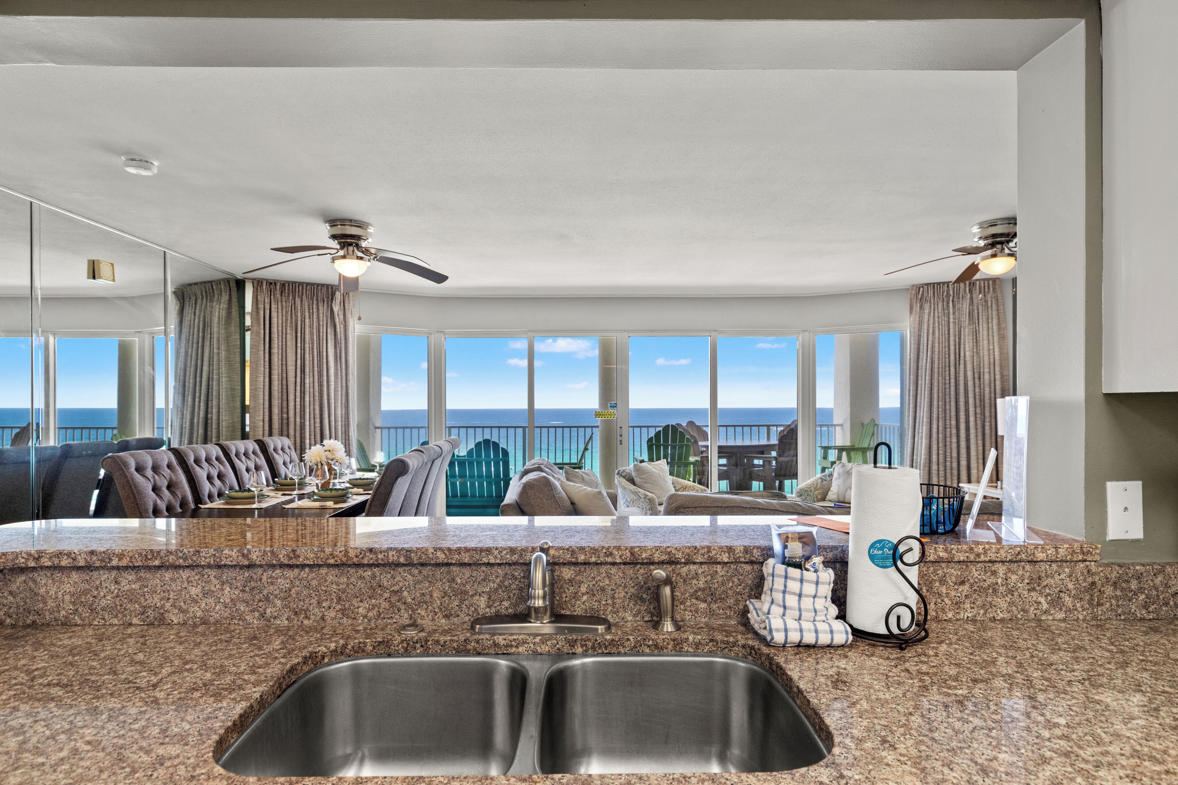 A modern kitchen with granite countertops, stainless steel sink, and ceiling fans.