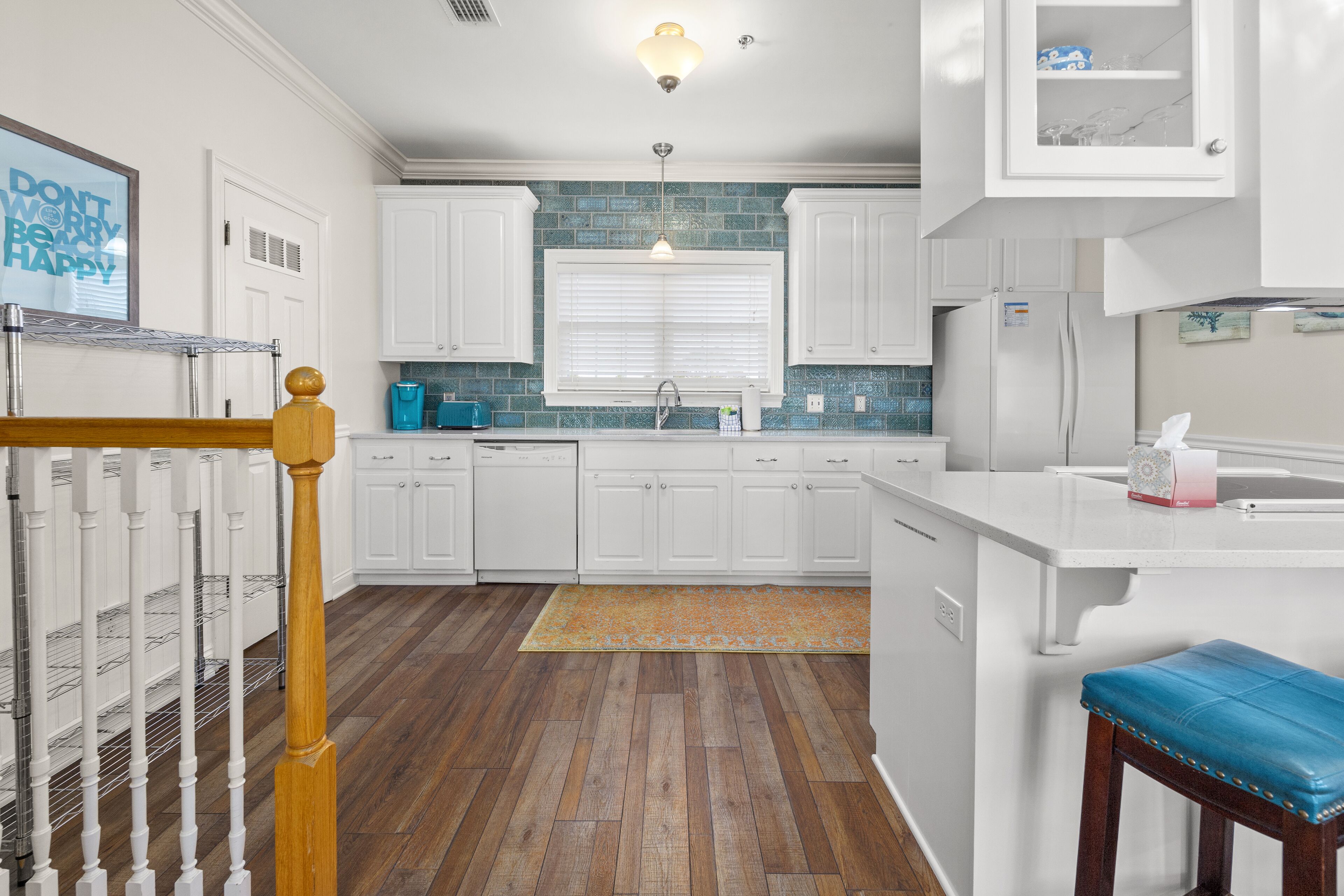 Een moderne keuken met witte kastjes, een houten vloer en een blauwe bank.