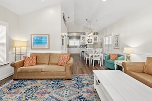 A spacious living room with a beige sofa, a patterned rug, and a dining area with white furniture. - Next To Pier Park! Steps From the Beach! Dog-friendly! Pool! (Panama City Beach)