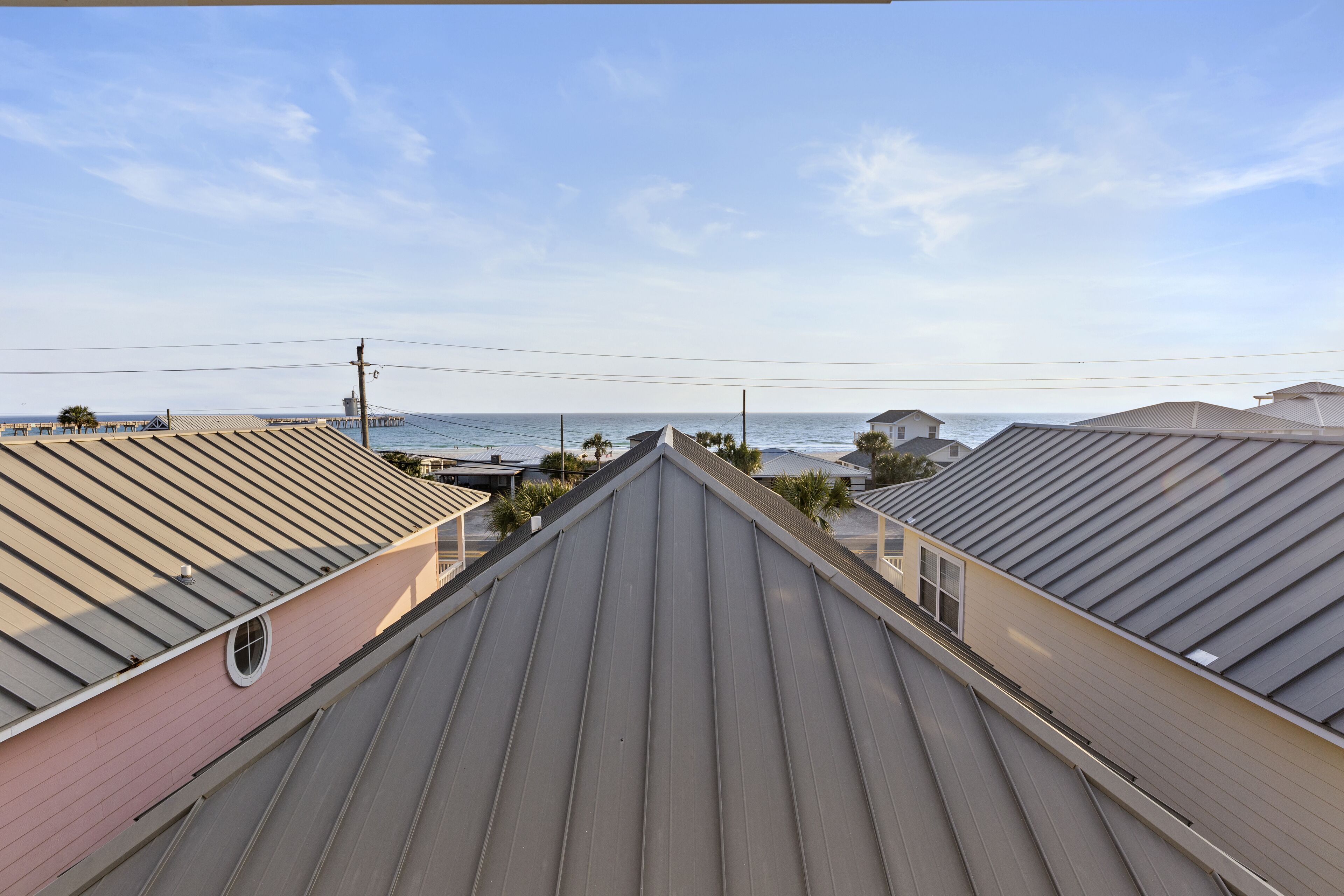 Vista de um bairro residencial com casas de telhados inclinados, céu claro e uma vista distante do oceano.