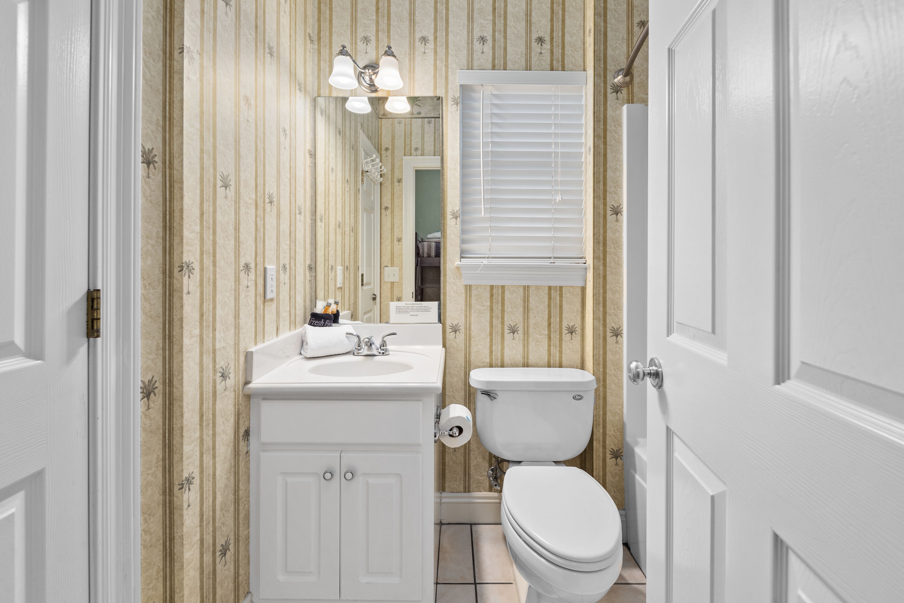 A bathroom with striped wallpaper, a white sink, a toilet, and a mirror with lights above it.
