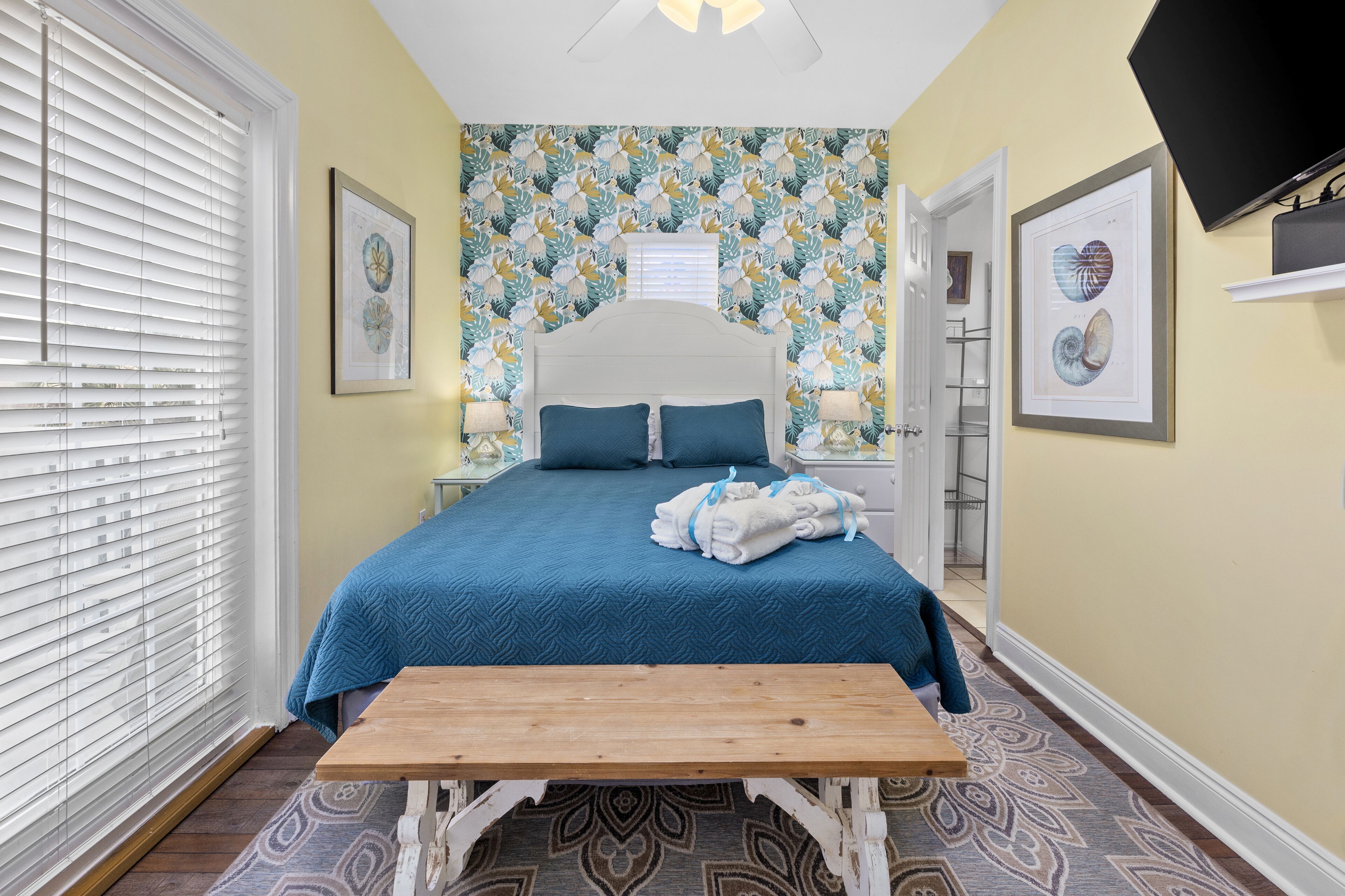 Une chambre à coucher comprenant un lit, des tables de chevet, un banc, un téléviseur et un tapis à motifs.