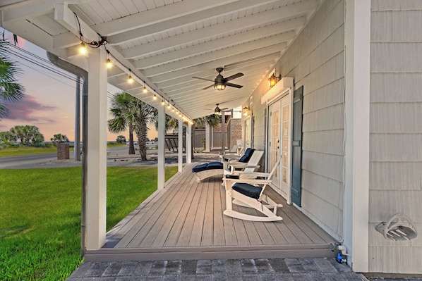A covered porch with a ceiling fan, string lights, and outdoor seating.
