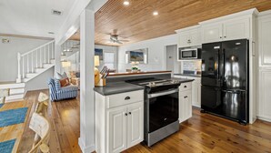 A kitchen with white cabinets, a black refrigerator, and a wooden ceiling. - Cute Beach Cottage Steps to the Beach! Panama City Beach, FL! (Panama City Beach)