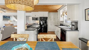 A modern kitchen with white cabinets, a black refrigerator, and a dining area with a wooden table and chairs. - Cute Beach Cottage Steps to the Beach! Panama City Beach, FL! (Panama City Beach)