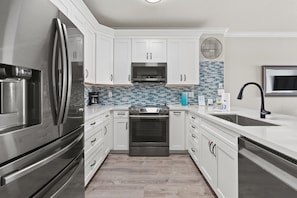 Fully equipped kitchen with stainless steel appliances, white cabinetry, and a tiled backsplash.