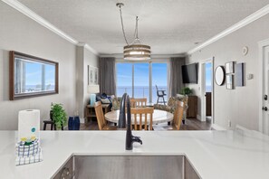 Una cocina moderna con una isla central, un comedor con una mesa redonda y sillas, y un gran ventanal con vistas al exterior.