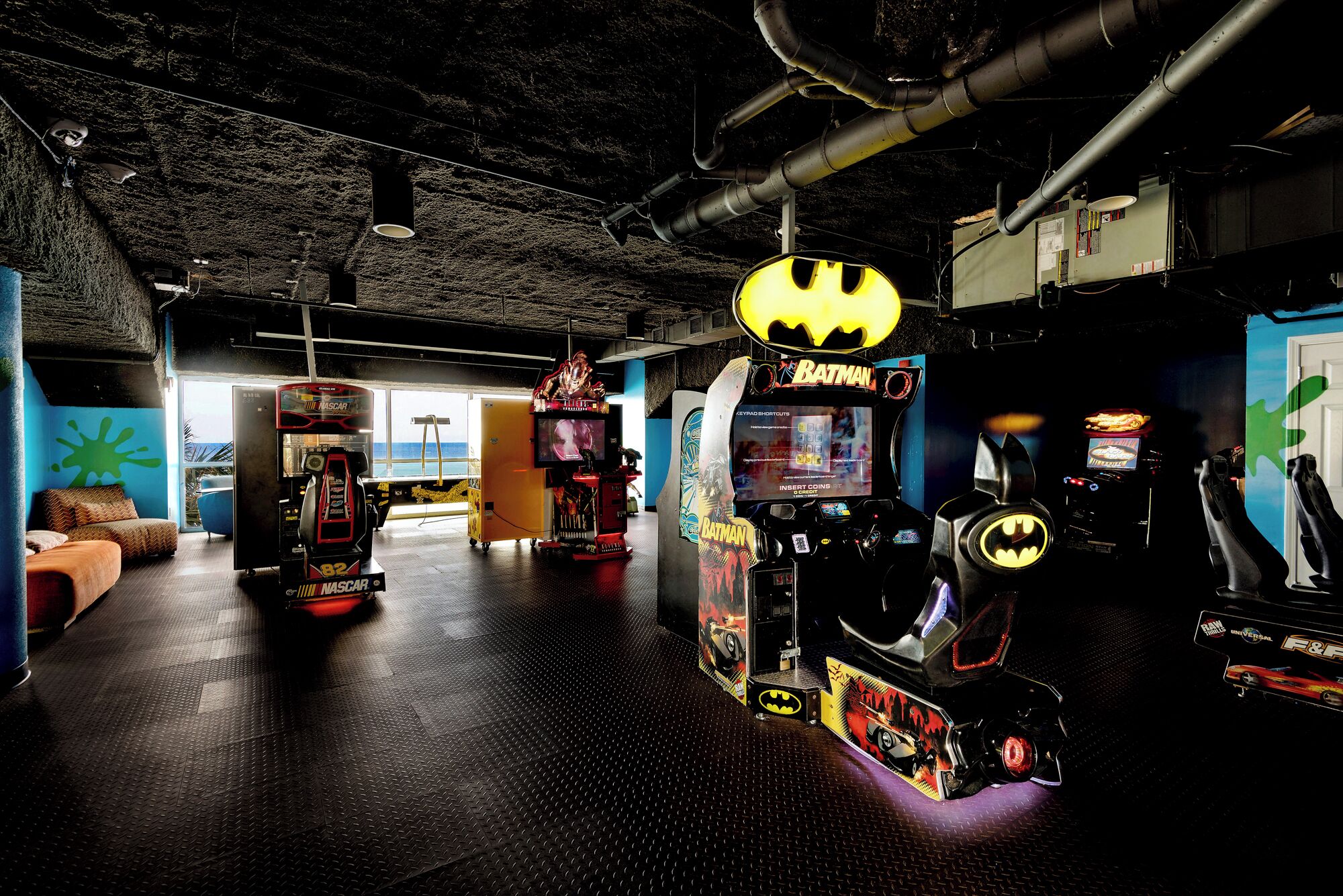 Un salón de juegos con varias máquinas, incluyendo una con temática de Batman y otra de carreras NASCAR.