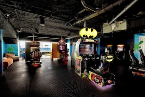 A gaming arcade with various machines, including a Batman-themed one, and a NASCAR racing machine. - Gulf Front! 2 BR 2 BA! 11th Floor Condo + Condo Amenities! (Panama City Beach)