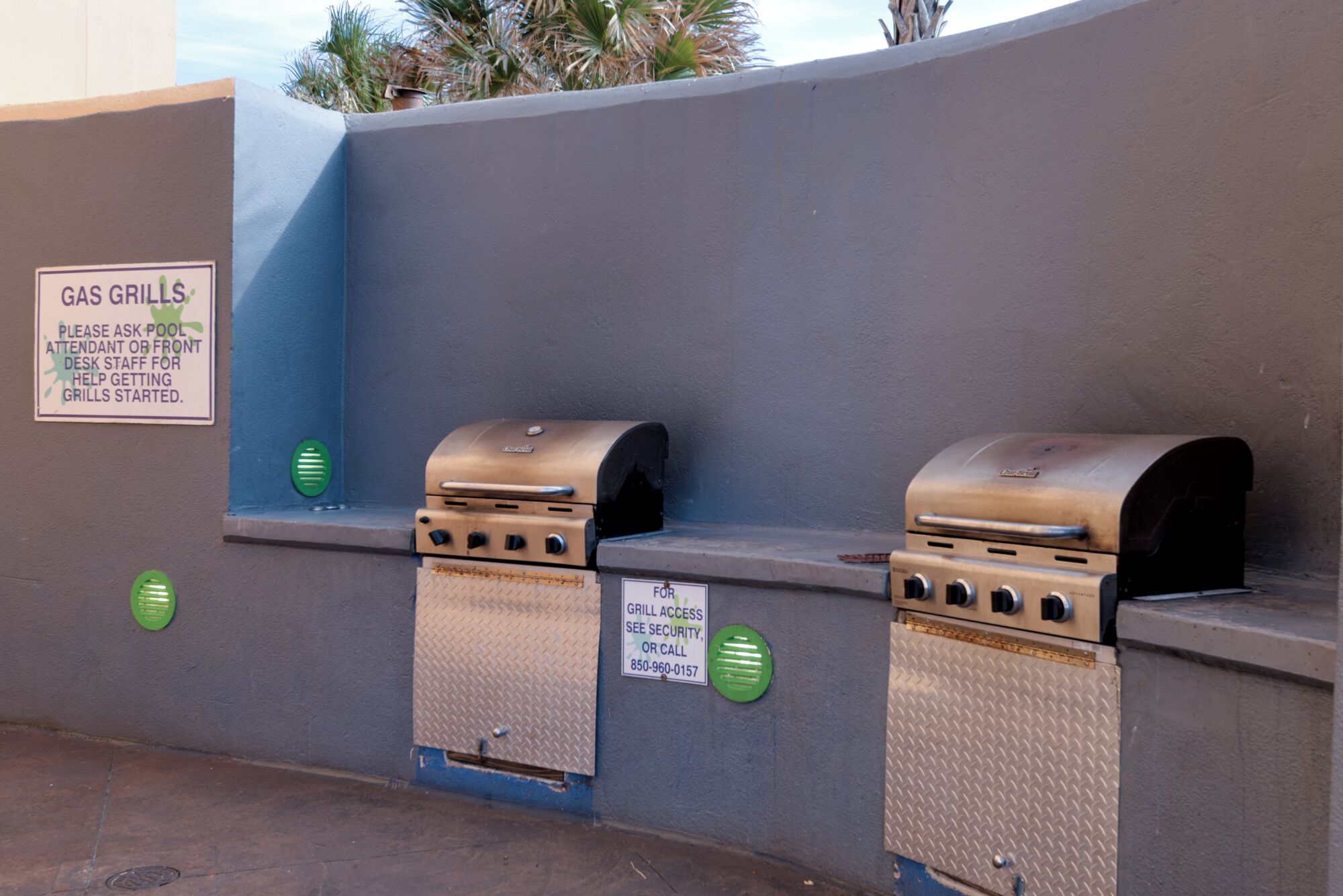 Zwei an einer Wand befestigte Gasgrills mit einem Schild, das den Zugang zum Grill und eine Kontaktnummer für Sicherheitsfragen anzeigt.